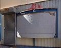 View of the front of an old abandoned shop with boarded up windows covering the storefront and a closed steel shutter Royalty Free Stock Photo