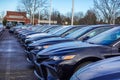 View of the fronts of a row of various colored new cars in a parking lot.