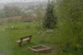 View of garden with bench through window with raindrops