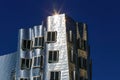 View on Gehry house with silver shiny futuristic metallic aluminium facade against blue sky, sun burst effect
