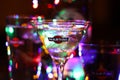 View on glass with martini cocktail with ice cube. Vibrant colorful bokeh background