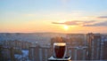 A view of a glass mug with hot black coffee on a blurred background of the rising sun and city skyline in an early spring morning Royalty Free Stock Photo