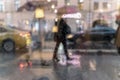 Blurry reflection silhouettes of the people in walking on a rain under umbrellas and bokeh city lights, night. View