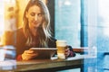 View through glass. Young smiling business woman sitting in cafe at table, drinking coffee and using tablet computer. Royalty Free Stock Photo