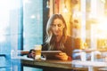 View through glass. Young smiling business woman sitting in cafe at table, drinking coffee and using tablet computer. Royalty Free Stock Photo