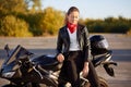 View of good looking young woman dressed in black jacket, has stylish red bandana on neck, dark hair comed in pony tail, stads nea Royalty Free Stock Photo