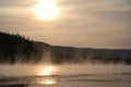 The view of Grand Prismatic Springs at sunset with mountains in the background and steam in front.