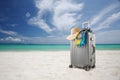 Gray suitcase with pareo and hat on tropical beach