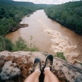 View from great height into abyss down, photo of river in gorge taken down from high cliff, photo shows photographer\'s legs,