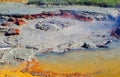 View on grey hot bubbling mud hole with red stones and yellow sulfuric ground