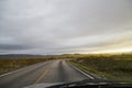 View on grey road, yellow surise and dramatic clouds from the car front window in early mourning. Driving car during sunshine in Royalty Free Stock Photo
