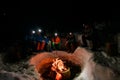 view of group of tourists sitting and bask around a campfire in winter evening. Royalty Free Stock Photo