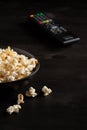 View of half a bowl with popcorn on dark table with remote control in the background, selective focus,