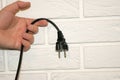 view of a hand holding a black 220v plug against a white brick wall