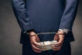 View of handcuffed businessman in suit holding bribe on grey Royalty Free Stock Photo