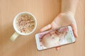 View handheld color video baby monitor. Female hands are holding a smartphone with a baby monitor app. Near hot drink Royalty Free Stock Photo