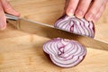 View on hands of a man chopping peeled fresh red onion for lunch an a bamboo cutting board. Royalty Free Stock Photo