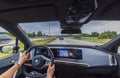View of hands of woman driving new BMW iX40 electric car driving along highway.