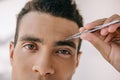 View of handsome man plucking eyebrows with tweezer and looking at camera Royalty Free Stock Photo