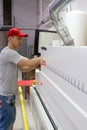 Industrial carpenter worker operating wood cutting machine during wooden door furniture manufacturing