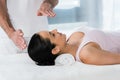 View of healer putting hands above head of brunette girl on massage table