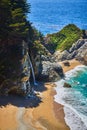 View of hidden waterfall from cliffs into sandy beaches by ocean waves