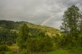 View of a high-mountainous small village in the forest. Rainbow over the mountains on a summer evening. Royalty Free Stock Photo