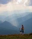 The view with the high mountains in fog. The sun rays are enlighten the forests. The extreme girl with the tracking sticks. Royalty Free Stock Photo