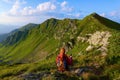 The view with the high rocky mountains. A young girl sits on the green grass among the flowers. Sun rays. Summer landscape. Royalty Free Stock Photo