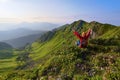 The view with the high rocky mountains. A young girl sits on the green grass among the flowers. Sun rays. Summer landscape. Royalty Free Stock Photo