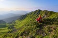 The view with the high rocky mountains. A young girl sits on the green grass among the flowers. Sun rays. Summer landscape. Royalty Free Stock Photo