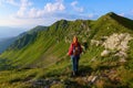 The view with the high rocky mountains. A young girl stands on the green grass among the flowers. Sun rays. Summer landscape. Royalty Free Stock Photo