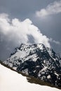 View of a high steep rocky mountain partially covered with snow against a dark cloudy sky with clouds clinging to the Royalty Free Stock Photo