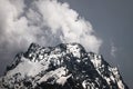 View of a high steep rocky mountain partially covered with snow against a dark cloudy sky with clouds clinging to the Royalty Free Stock Photo