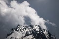 View of a high steep rocky mountain partially covered with snow against a dark cloudy sky with clouds clinging to the Royalty Free Stock Photo