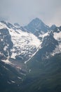 View of a high steep rocky mountain partially covered with snow against a dark cloudy sky with clouds clinging to the Royalty Free Stock Photo