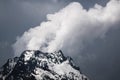 View of a high steep rocky mountain partially covered with snow against a dark cloudy sky with clouds clinging to the Royalty Free Stock Photo