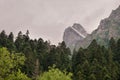 View of a high steep rocky mountain partially covered with snow against a dark cloudy sky with clouds clinging to the Royalty Free Stock Photo