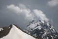 View of a high steep rocky mountain partially covered with snow against a dark cloudy sky with clouds clinging to the Royalty Free Stock Photo