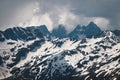 View of a high steep rocky mountain partially covered with snow against a dark cloudy sky with clouds clinging to the Royalty Free Stock Photo