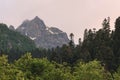 View of a high steep rocky mountain partially covered with snow against a dark cloudy sky with clouds clinging to the Royalty Free Stock Photo