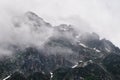 View of a high steep rocky mountain partially covered with snow against a dark cloudy sky with clouds clinging to the Royalty Free Stock Photo