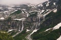 View of a high steep rocky mountain partially covered with snow and waterfalls against a dark cloudy sky with clouds Royalty Free Stock Photo