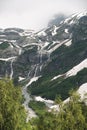 View of a high steep rocky mountain partially covered with snow and waterfalls against a dark cloudy sky with clouds Royalty Free Stock Photo