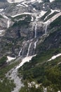 View of a high steep rocky mountain partially covered with snow and waterfalls against a dark cloudy sky with clouds Royalty Free Stock Photo