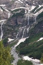 View of a high steep rocky mountain partially covered with snow and waterfalls against a dark cloudy sky with clouds Royalty Free Stock Photo