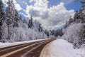 View of highway running alongside winter forest covered in snow, with road markers against backdrop of blue sky with white clouds. Royalty Free Stock Photo