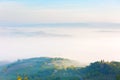 View of hilly fields of Tuscany in the light of the rising sun in autumn foggy morning, Italy