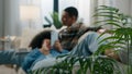 View through house plant African American happy family couple relaxing on couch man working playing game with laptop Royalty Free Stock Photo