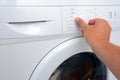 View on how a man is turning on of the washing machine. A man is choosing a washing mode on the washing machine.